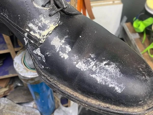 Zapato negro de vestir manchado de pintura y con la piel muy desgastada